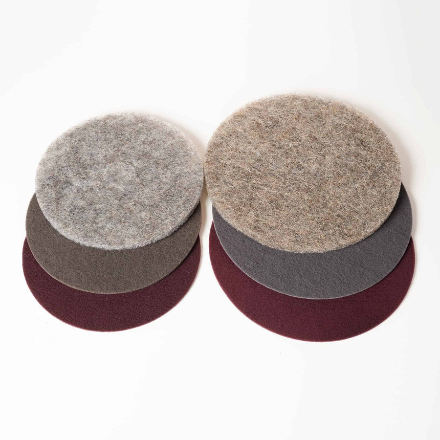 Photo shows two sets of three scrubbing pads. On the bottom layer of each set is a maroon pad. Laid over that is a grey pad and laid over that is a natural scrubbing pad.